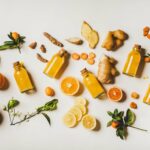 Bottled immunity juices, oranges, lemons, turmeric, and ginger spread out on a table.