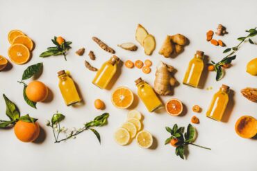 Bottled immunity juices, oranges, lemons, turmeric, and ginger spread out on a table.