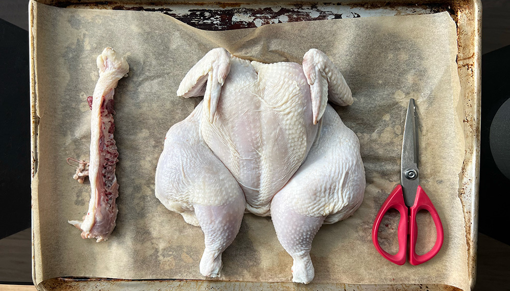 A spatchcocked chicken on a baking sheet.