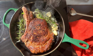 Bone-in Ribeye Steak searing in a cast iron skillet with garlic and herbs.